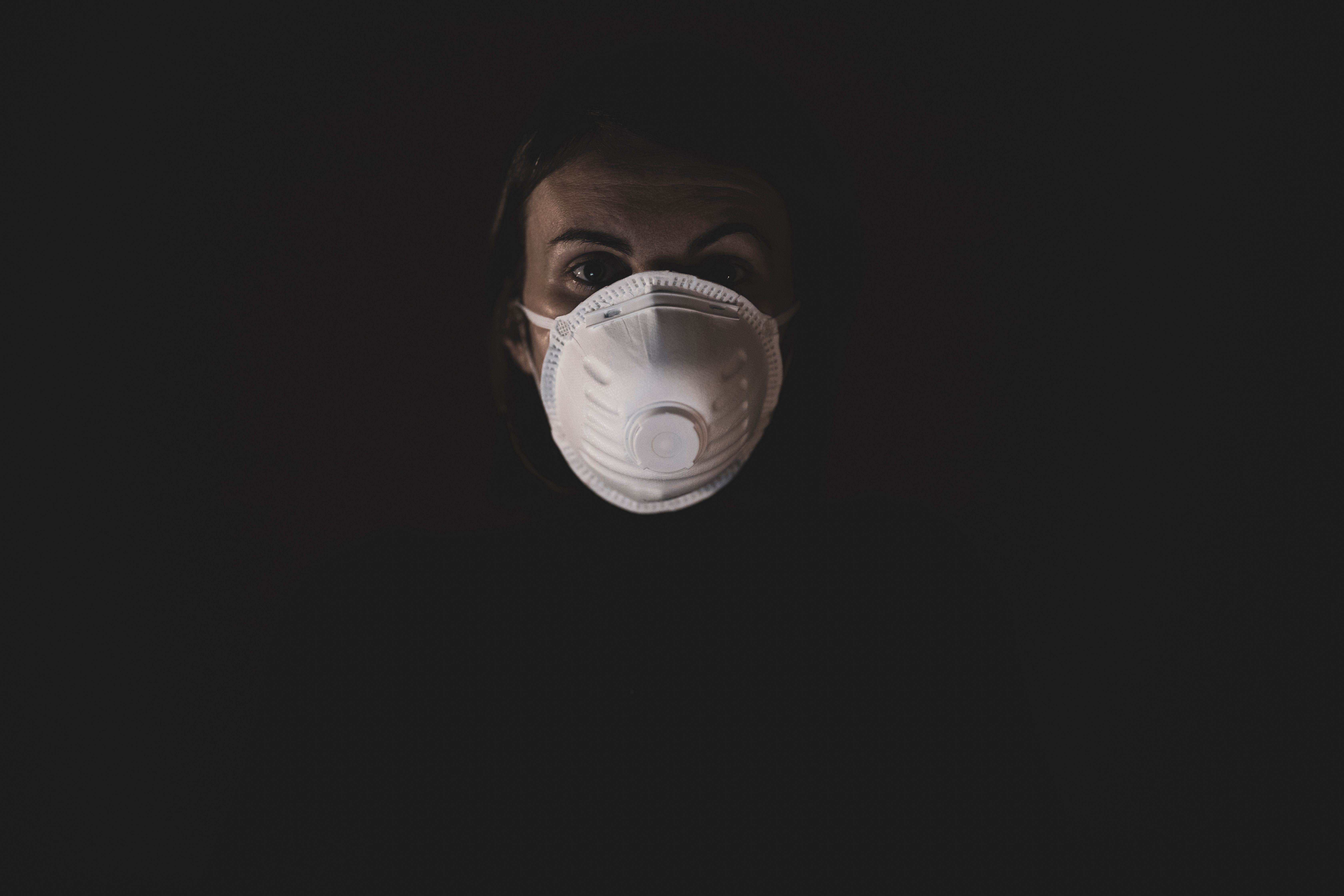 A person wearing an N95 mask in a dimly lit environment, emphasizing safety during the pandemic. A person wearing an N95 mask in a dimly lit environment, emphasizing safety during the pandemic.