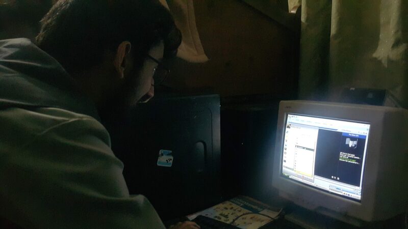 Man hunched over computer in darkness
