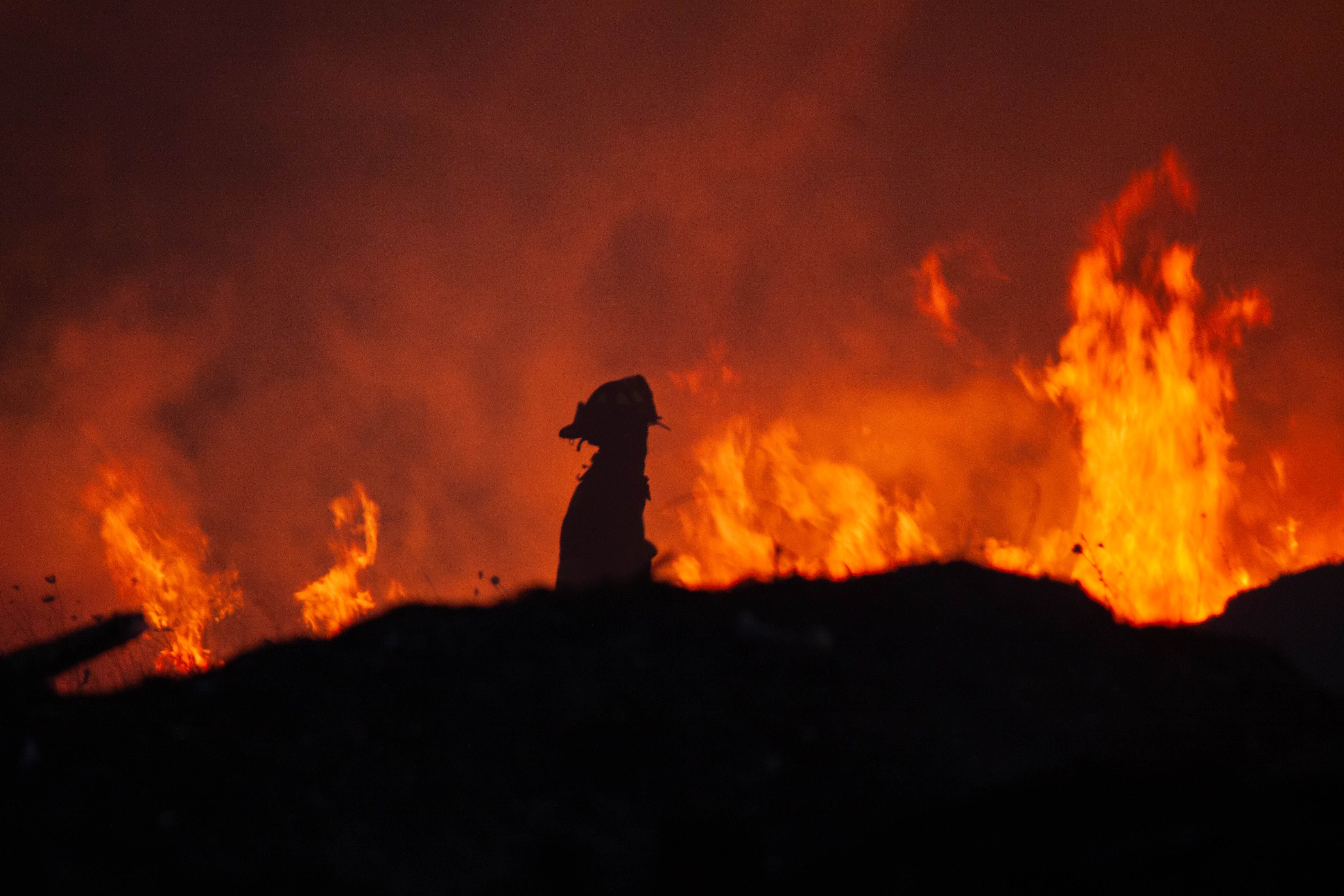 firefighter against a blazing fire at night A dramatic silhouette of a firefighter against a blazing fire at night, emphasizing bravery and action.