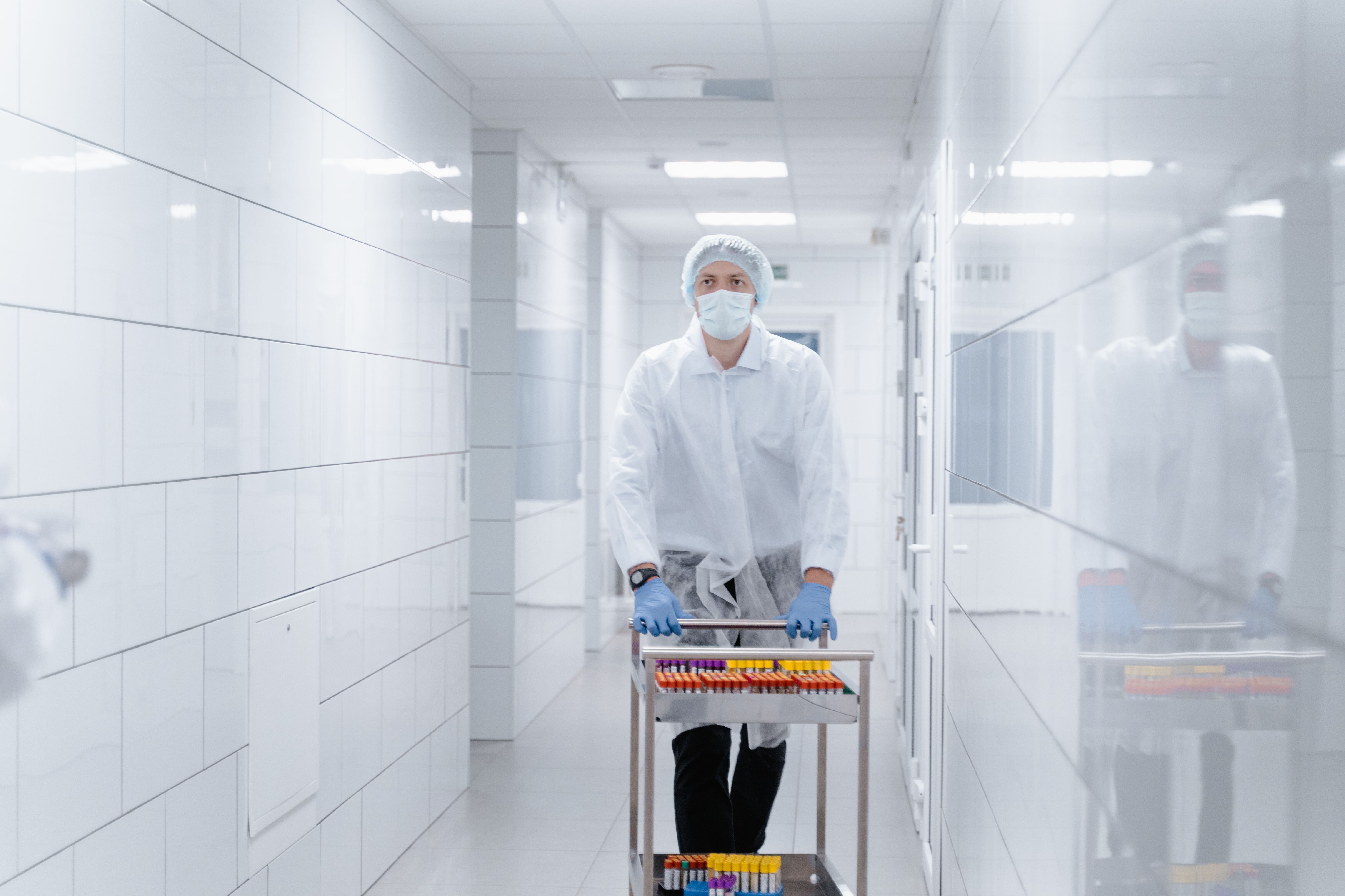 Lab technician Lab technician in protective gear transporting samples in a sterile laboratory hallway.