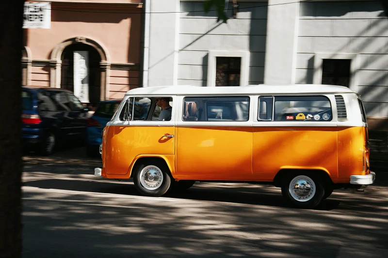 A classic yellow van drives past urban architecture in Hungary, embodying retro travel vibes.