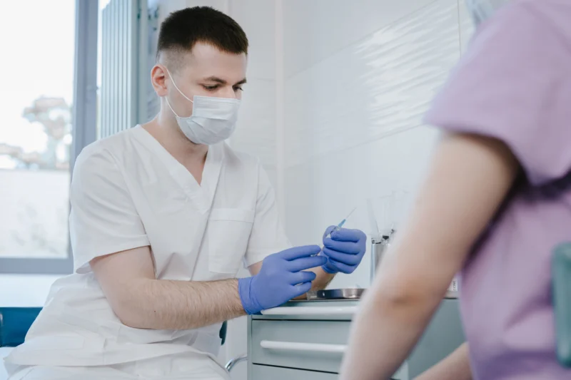 Healthcare worker in protective gear preparing a syringe for vaccination indoors.