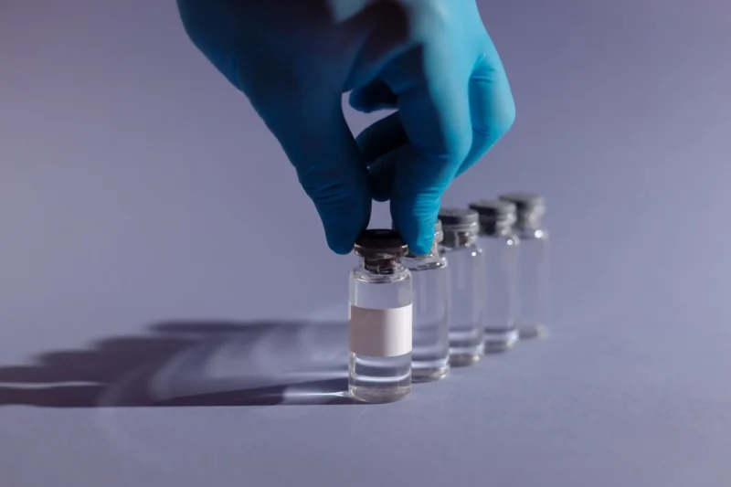 Healthcare worker with gloves handling vaccine vials in a sterile environment.