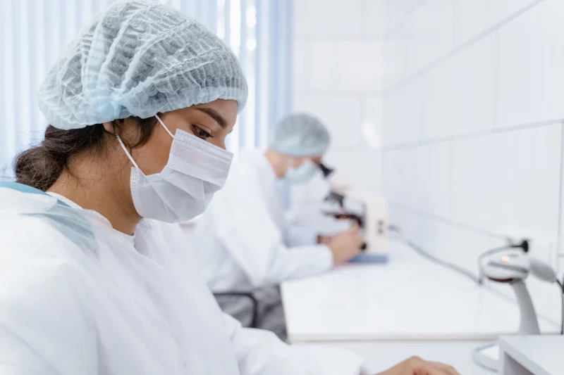 Two lab technicians wearing masks and protective gear working in a laboratory setting.